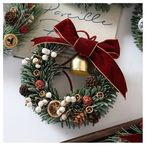 Detail of Christmas wreath with red velvet bow, gold bells and pine cones on white background
