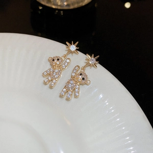 Macro detail of gold teddy bear earrings with pavé crystals and sparkling star studs