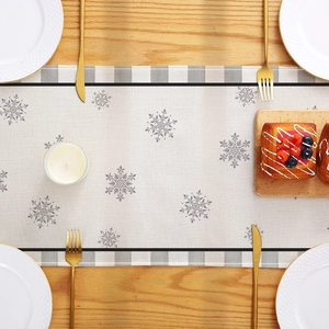 Christmas table runner with gray snowflakes and plaid borders on a wooden dining table