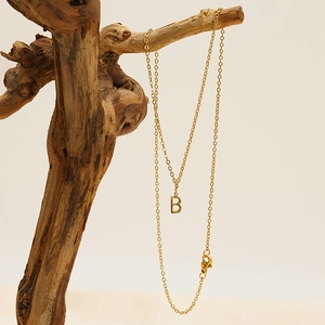 Detailed view of gold letter B pendant necklace on a natural branch against a beige backdrop