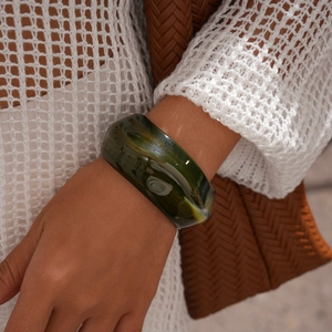 Detail of wide green acrylic resin bangle with marbled pattern on model's wrist