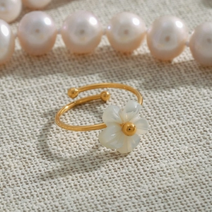 Close-up of a gold adjustable flower ring with white petals on beige textured fabric