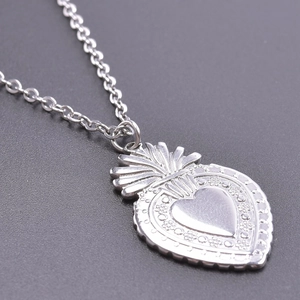 Détail macro du pendentif coeur sacré en argent avec rayons et reliefs floraux