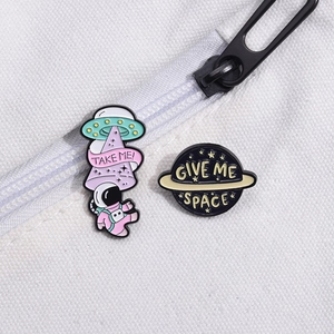 Cartoon astronaut and planet enamel pins featuring UFO and Saturn designs on white fabric