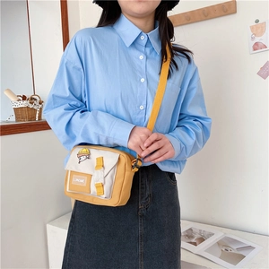 Side view of a yellow and white nylon crossbody bag with adjustable strap and pin detail
