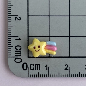 Mini yellow star resin charm with smiley face and rainbow tail on measuring mat