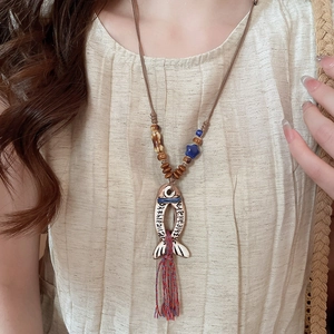 Detail of vintage fish pendant necklace with ceramic beads and tassel on model