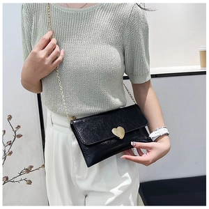 Detail of black mini crossbody bag featuring a golden heart clasp and chain strap