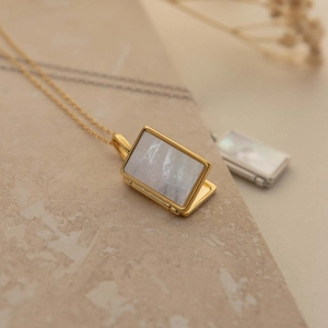 Close-up of golden rectangular locket necklace with iridescent white shell inlay detail