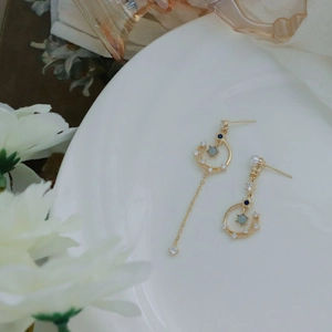 Detail of asymmetric gold earrings with green stones and pearls on white plate