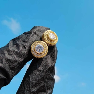 Macro shot of gold hip hop stud earring with clear zircon inlay held by a black gloved hand