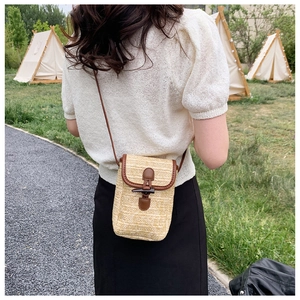 Outdoor shot of a woven straw mini crossbody bag with leather trim and horn toggle closure