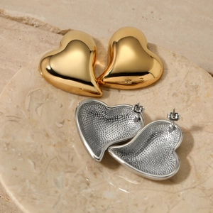 Polished asymmetrical gold and silver heart earrings displayed on marble tray