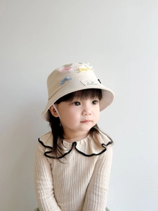 Detail of children's beige cotton sun hat featuring colorful 3D bow and logo patch