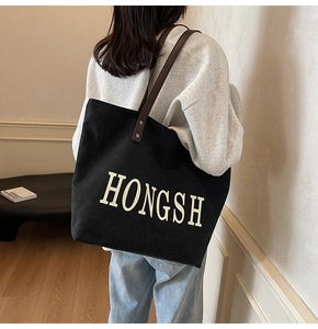 Model wearing large black canvas tote bag with leather straps and HONGSH text print