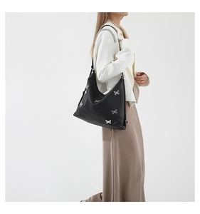 Detail of black shoulder bag with silver butterfly charms and chain strap on model