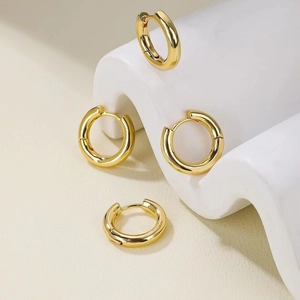 Polished gold stainless steel hoop earrings displayed on white geometric props