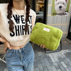 Close-up of green fleece cosmetic bag with white text patch held against gray wall