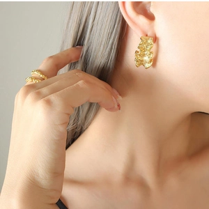 Detail of gold-plated irregular wavy earrings and matching textured ring on model