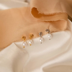 Detail of drop pearl earrings in gold and silver finishes on elegant silk fabric