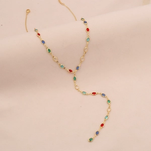 Elegant gold Y-shaped necklace with colorful oval crystals on soft pink fabric background