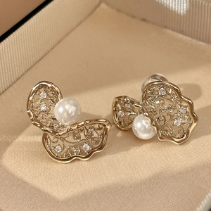 Close-up of gold twist flower earrings with pearl and zircon inlay on beige lining
