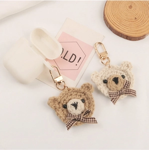 Cute knitted bear keychain charms with plaid bows next to white silicone earphone case