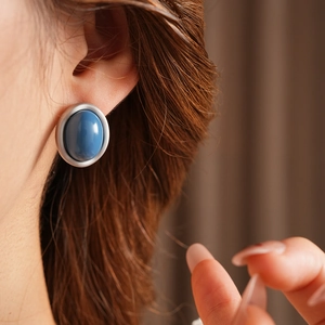 Close-up of elegant silver earrings with a blue oval gemstone worn by a model