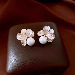 Macro shot of gold-plated floral earrings with white enamel petals and elegant drop pearl