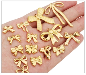 Golden stainless steel bow pendants in various sizes held in hand for jewelry DIY