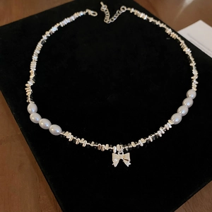 Détail du pendentif nœud argenté avec perles irrégulières sur velours noir chic