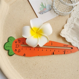 Detailed top view of a 6cm frangipani flower hair clip measured on a carrot ruler