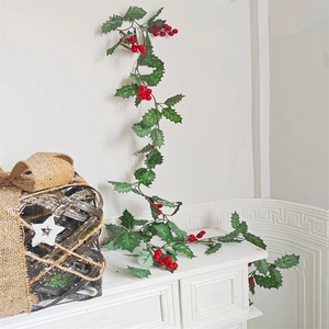 Artificial Christmas garland with green holly leaves and red berries on a white fireplace