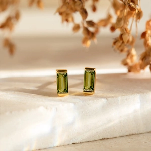 Macro detail of gold-plated square green zircon earrings with emerald-cut stones