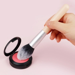 Close-up of a wooden handle makeup brush picking up pink powder from a black compact case