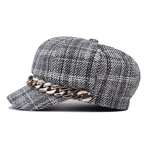 Close-up of houndstooth baker boy hat with decorative gold chain and tweed fabric texture