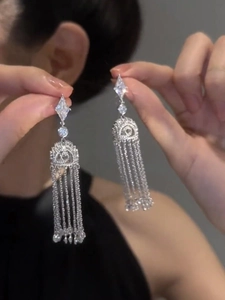 Close-up of diamond-studded geometric tassel earrings with silver chain details