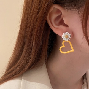 Close-up of a floral daisy earring with a yellow hollow heart pendant worn by a model