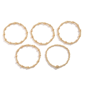 Detailed view of five layered gold metal bead bracelets in various sizes on white background