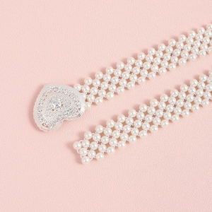 Close-up of pearl waist chain featuring a sparkling rhinestone heart buckle on pink background