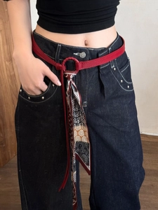 Detail of red leather belt with vintage silk scarf tied to metal ring on jeans