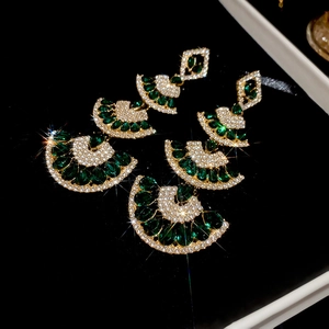 Macro detail of emerald green pear-cut stones and fan-shaped gold fringe earrings