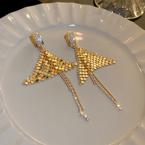 Detailed view of golden fish tail earrings with rhinestone tassels on a ceramic plate