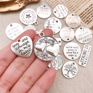 Hand holding silver inspirational quote charms in various shapes for DIY jewelry making