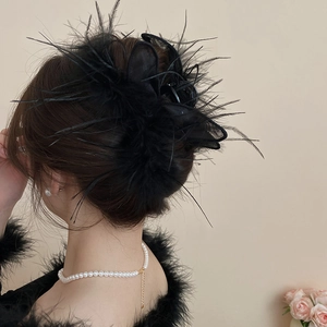 Detail of elegant black feather hair claw clip on model's bun with luxury pearl necklace