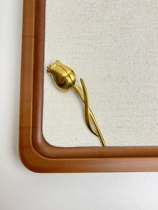 Detailed flat lay of golden tulip brooch pin with leaf on beige textured fabric