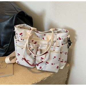 Detail of white canvas tote bag with cherry print and multi-pocket zipper design on stone