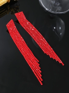 Close-up of long red rhinestone tassel earrings on a reflective black background