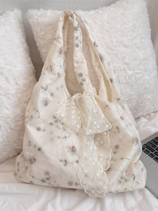 Floral embroidered tote bag with lace bow detail shown on a cozy white bed background