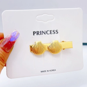 Detailed view of a gold double shell hair clip on a display card for beach styling